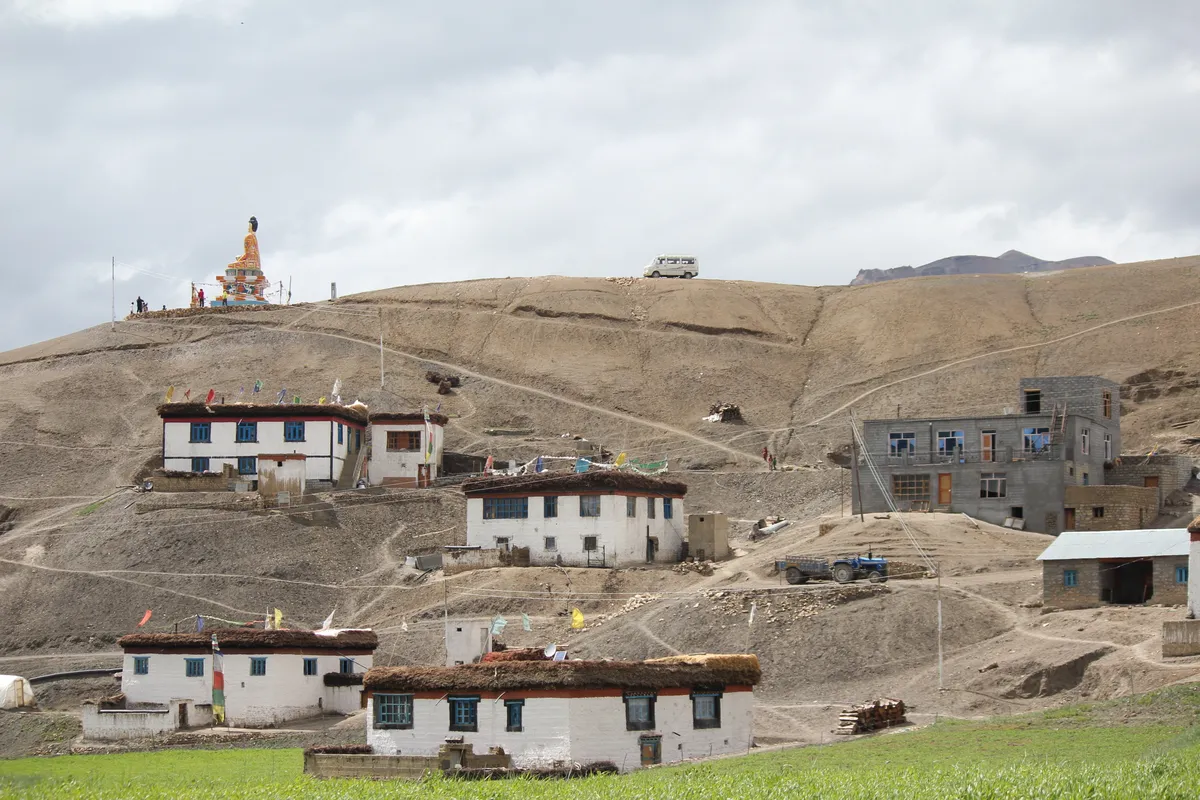 Whitewashed houses of Langza village with green fields and the Buddha statue on the ridge